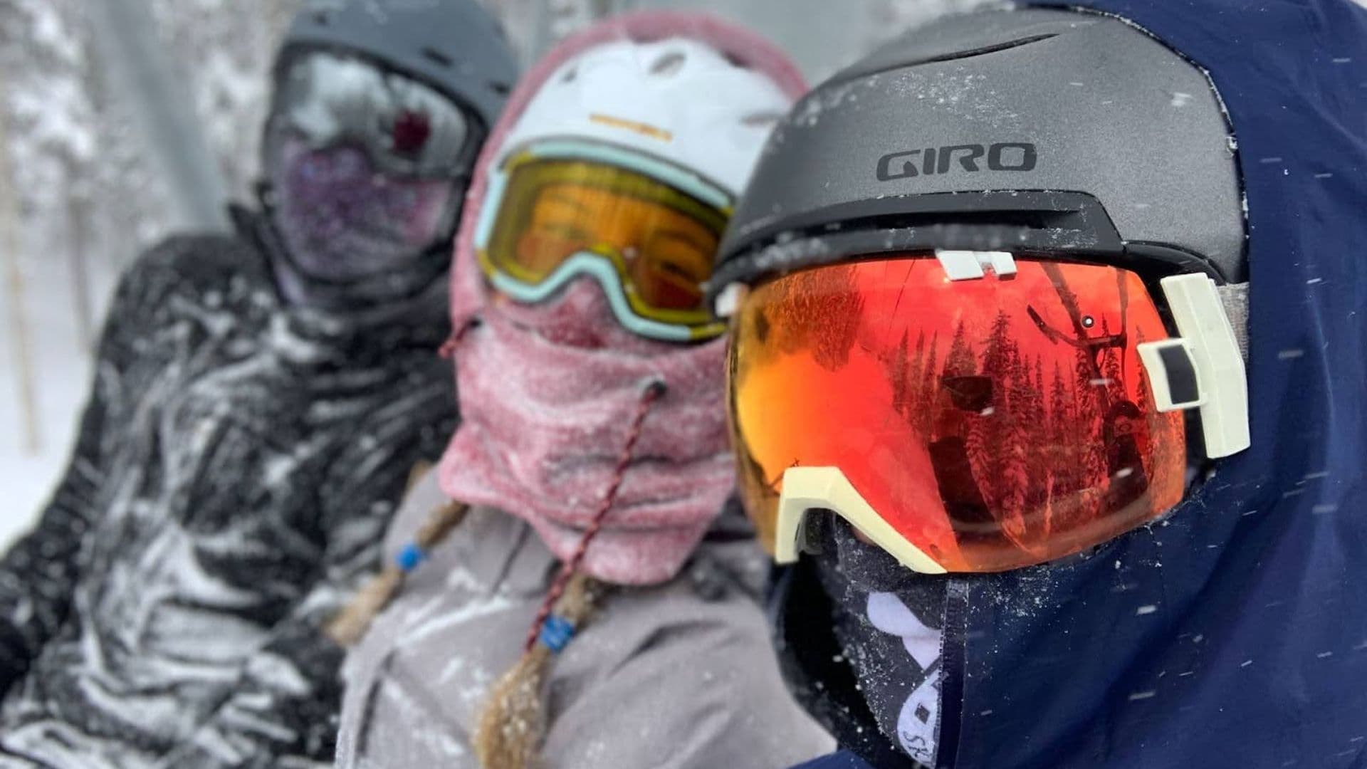 Three skiers on a chairlift while it's snowing