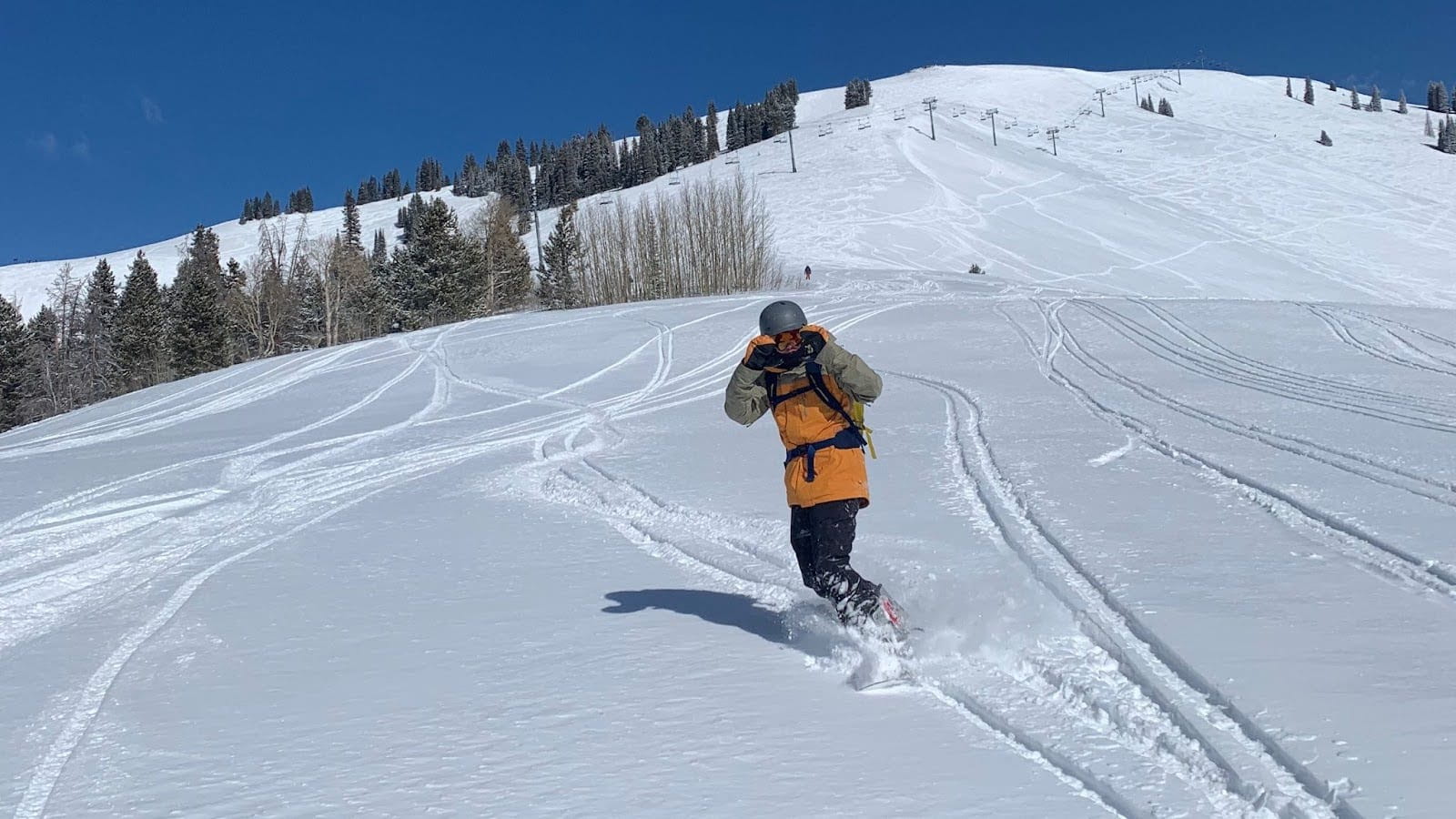 A snowboarder finds fresh powder with an open slope and a chairlift visible behind