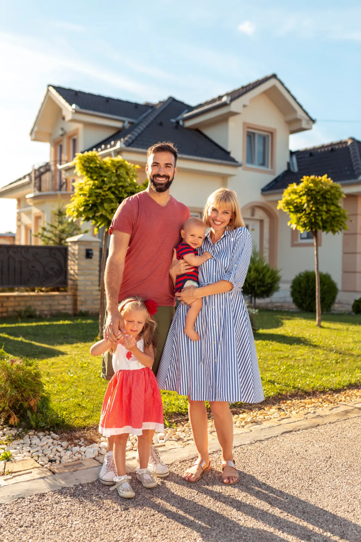 a family of 4 posing for a photo standing in front of their newly purchased home 