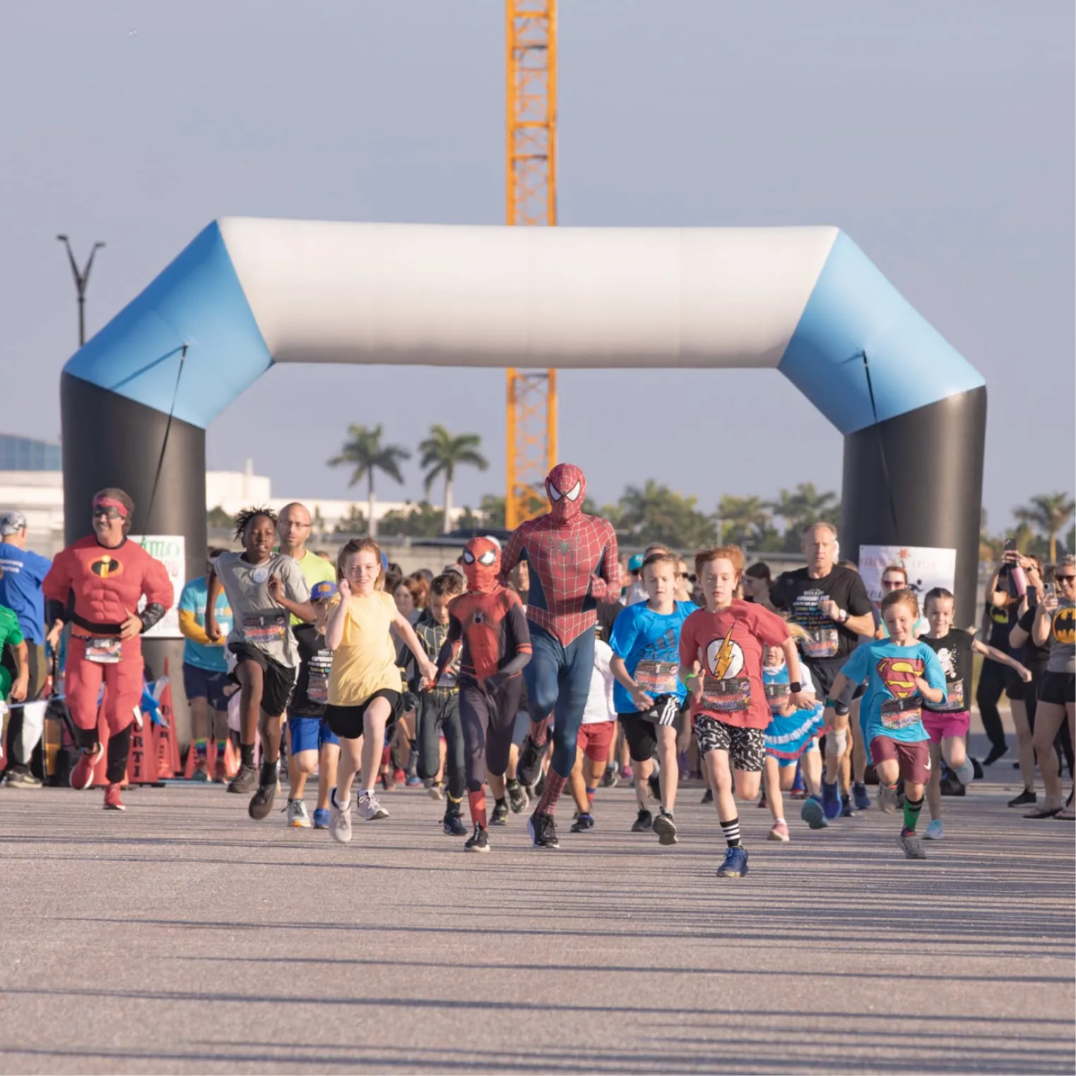 Adults and children in super hero costumes running toward the camera at a race