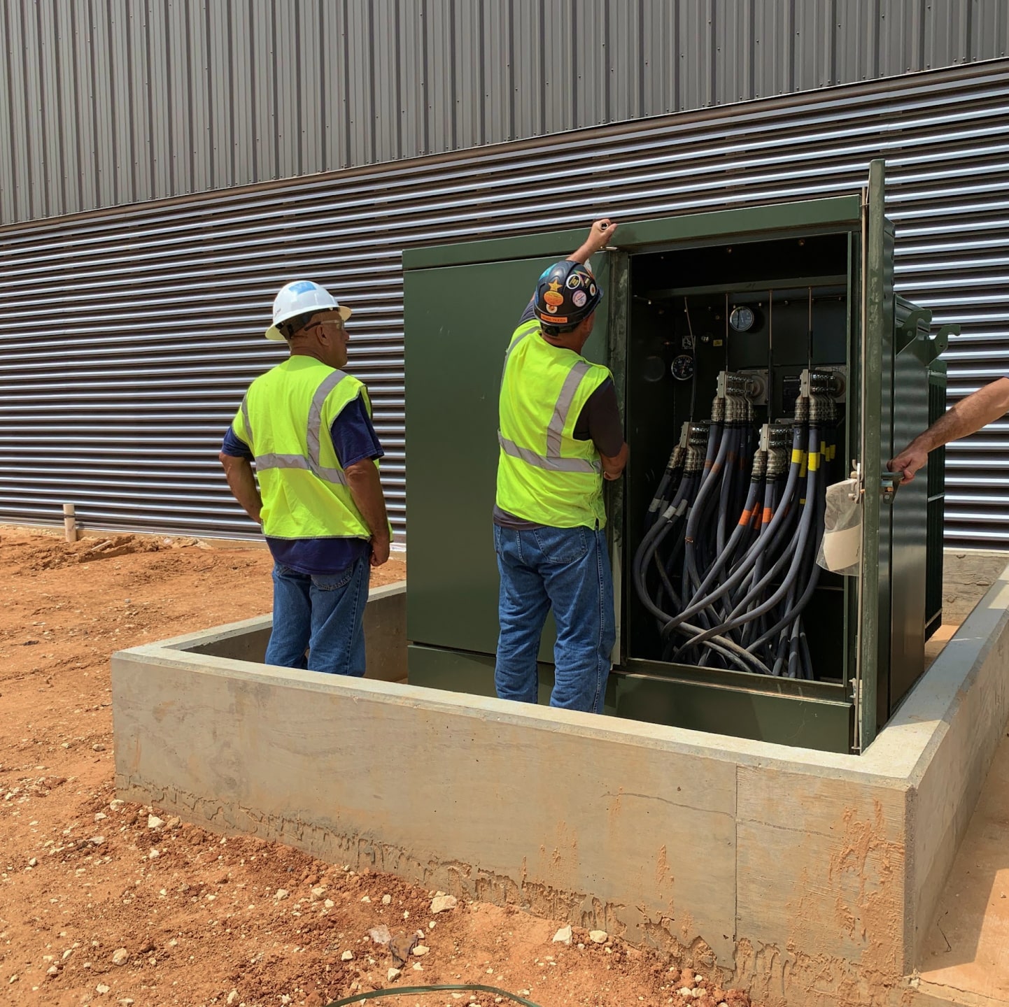 Two electricians installing a green Maddox padmount transformer.