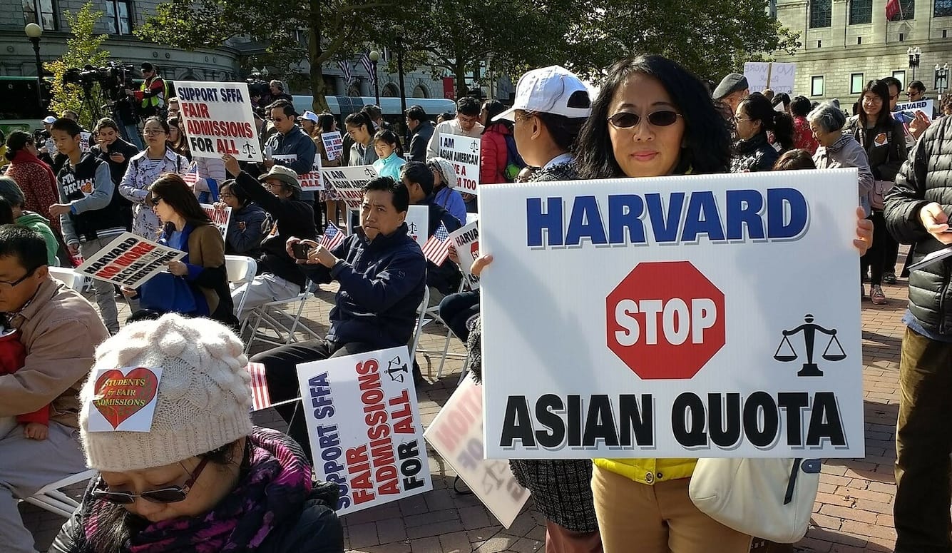 Protestors with placards. A young Asian woman holds a sign saying Harvard Stop Asian Quota.