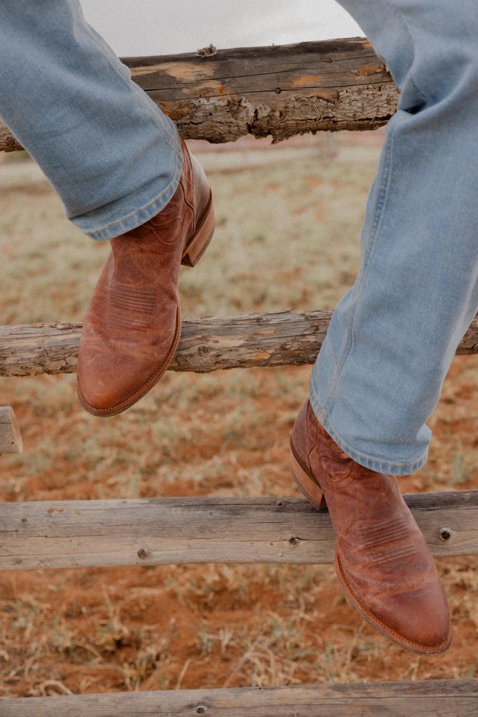 Closeup of man wearing boots sitting on a fence at a Ranch