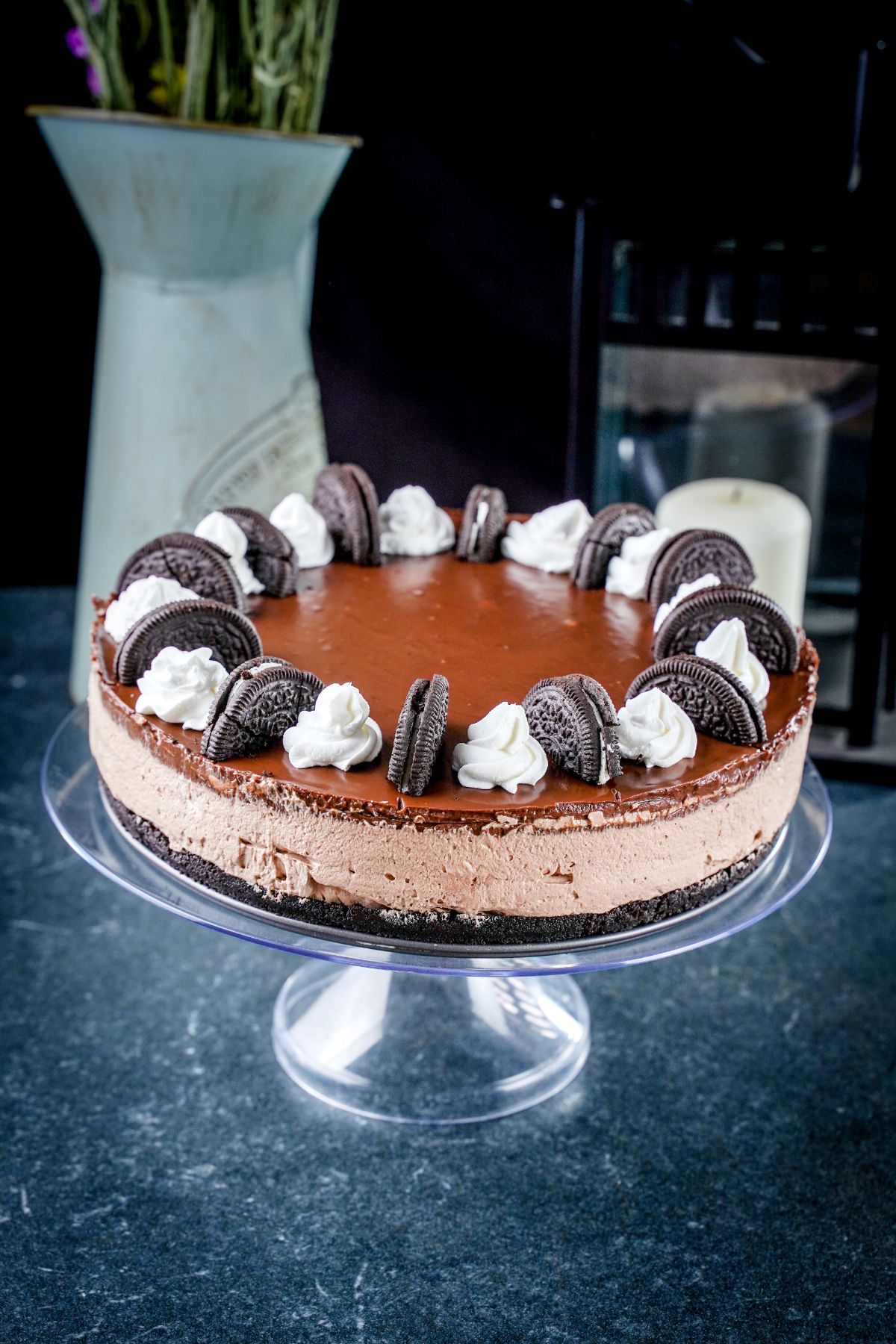 chocolate cheesecake on glass cake stand topped with Oreo cookies