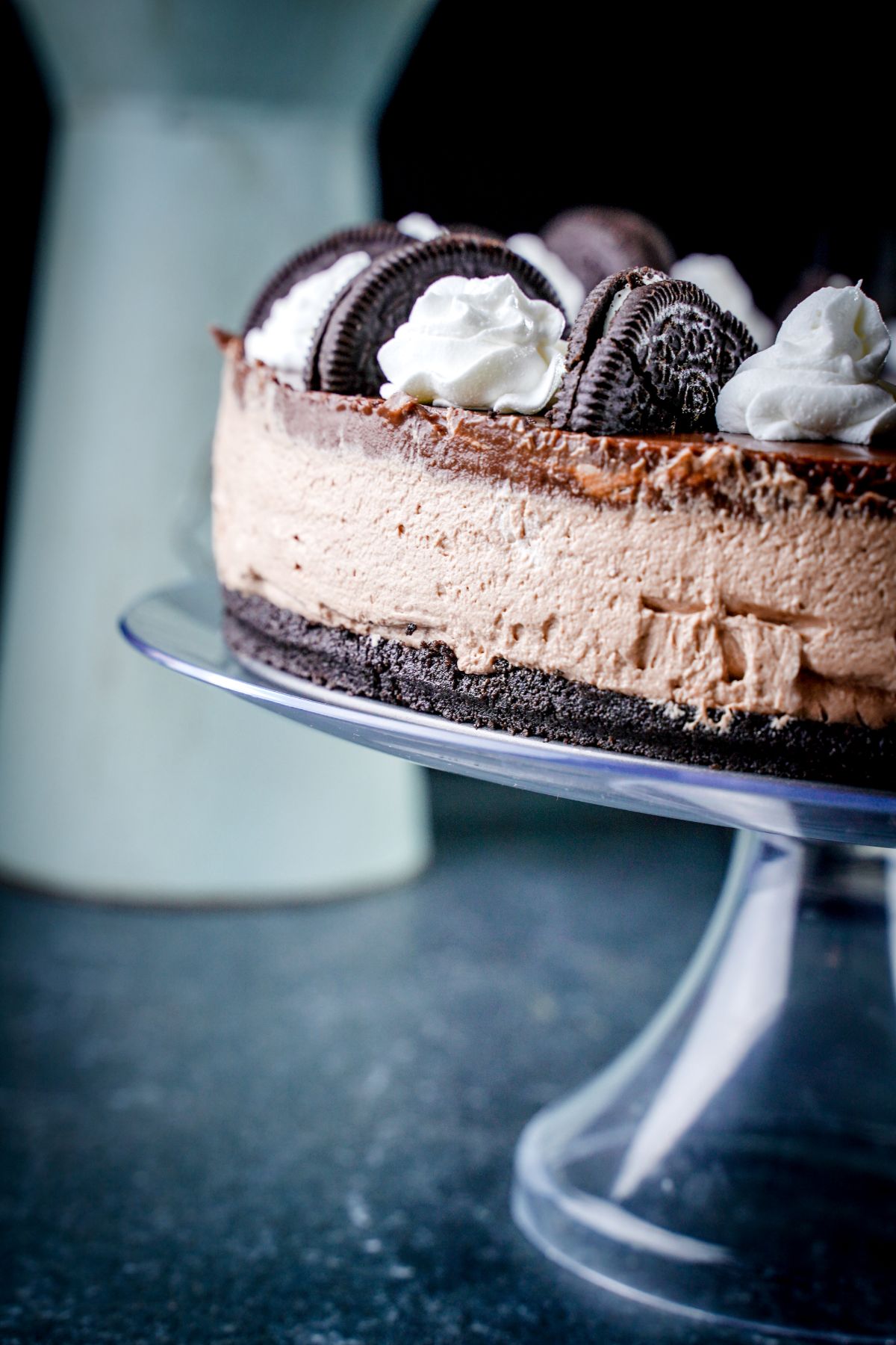 cake stand showing chocolate cheesecake with vase in the background