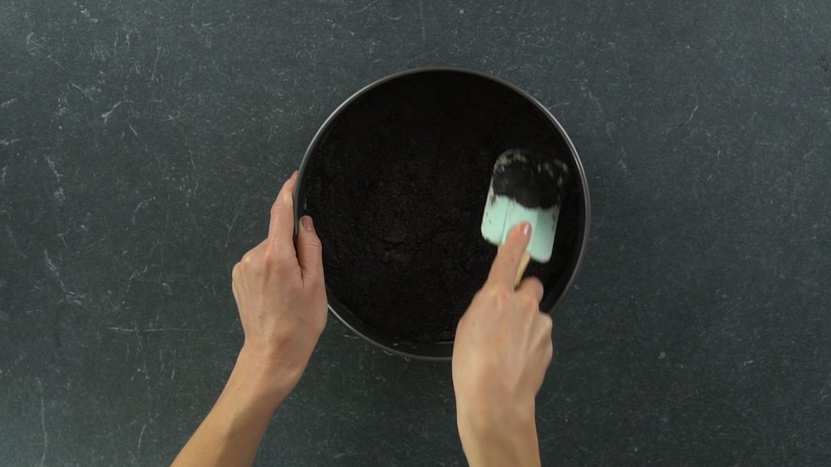 hand using blue spatula to press cookies into springform pan