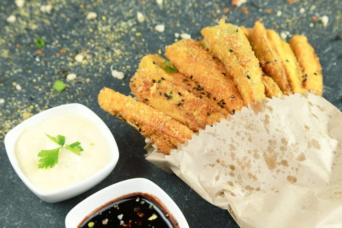 dipping sauce in white bowls next to fried eggplant in paper bag