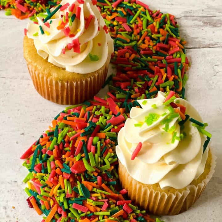 two cupcakes with white icing and sprinkles on table