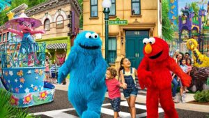 Close up of Elmo and the Cookie Monster walking with kids on Sesame Street plus Big Bird and Zoey in the background with more kids and families at Sesame Place San Diego in San Diego, California, USA