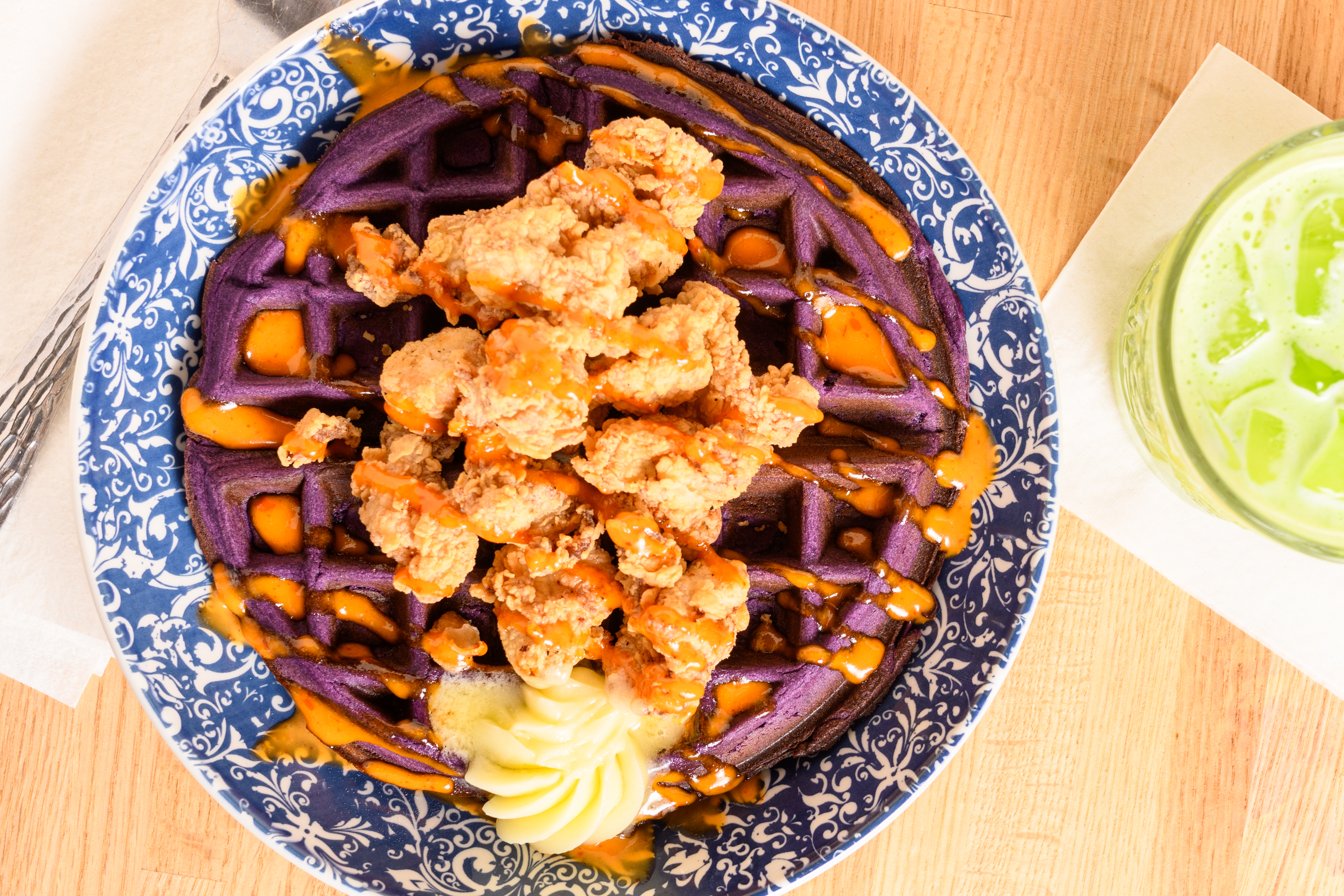 A purple waffle topped with fried chicken and drizzle.