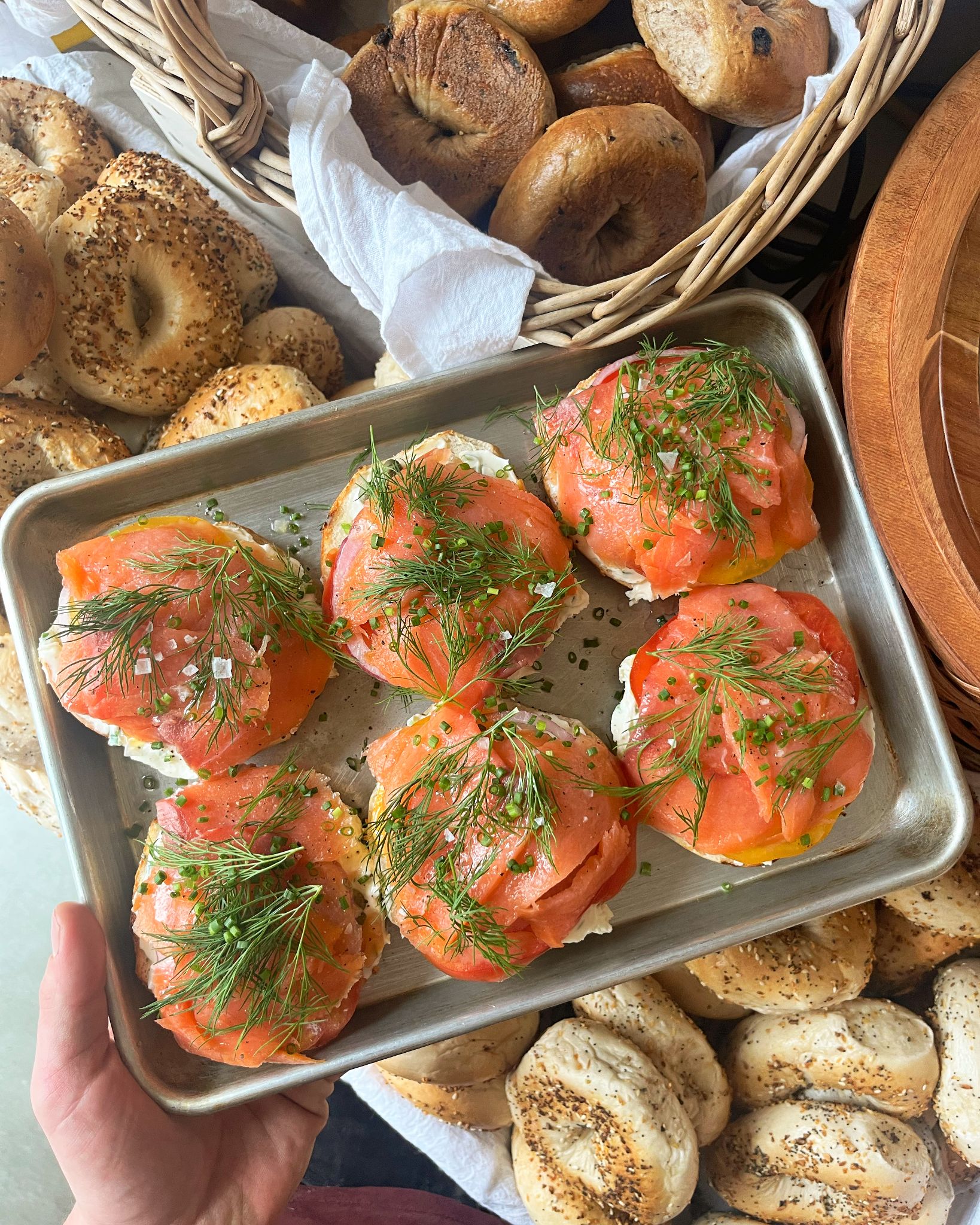 A metal tray of sliced bagels topped with cream cheese, tomato, lox, and dill.