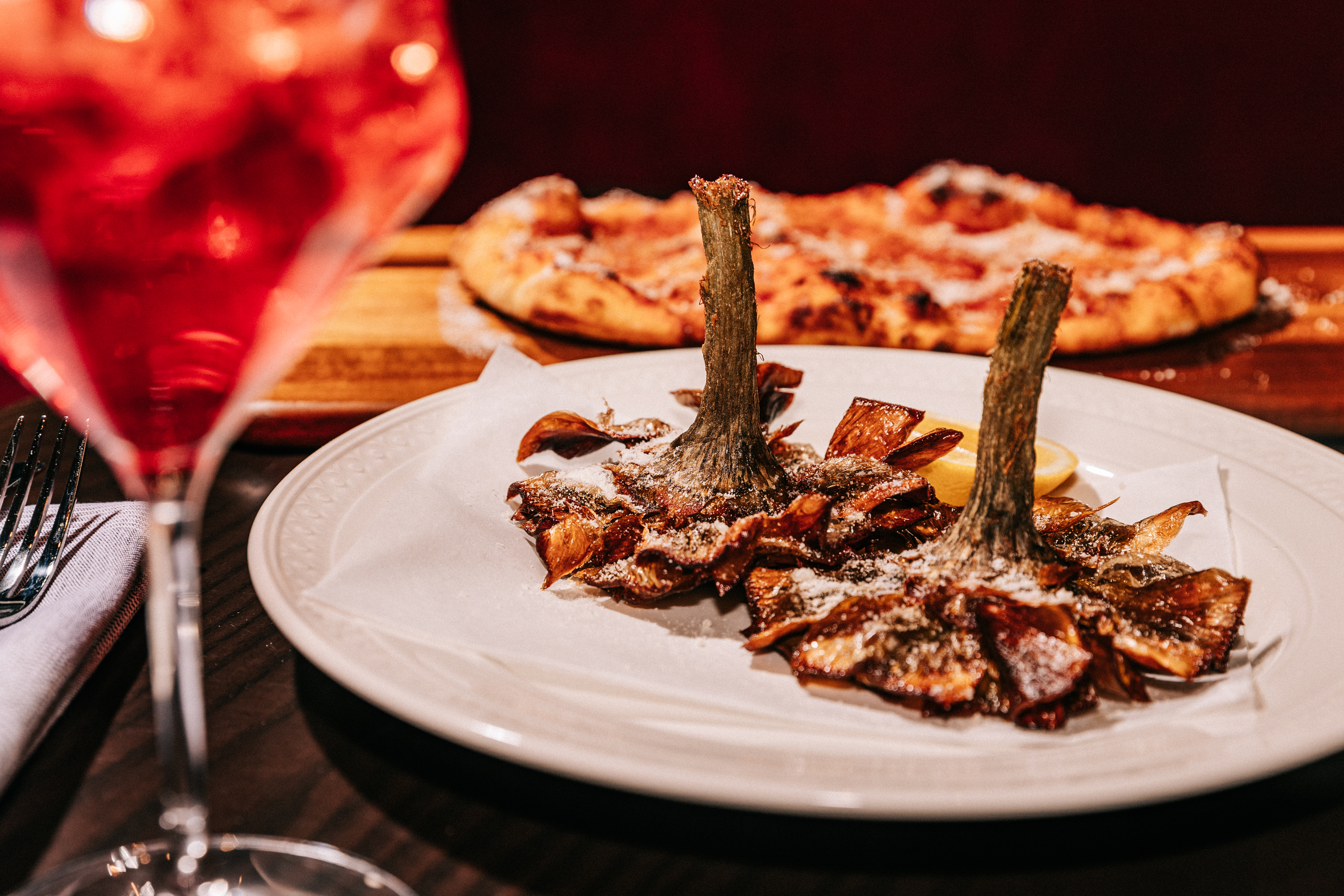 Two artichokes on a plate with a pizza in the background at Il Carciofo.