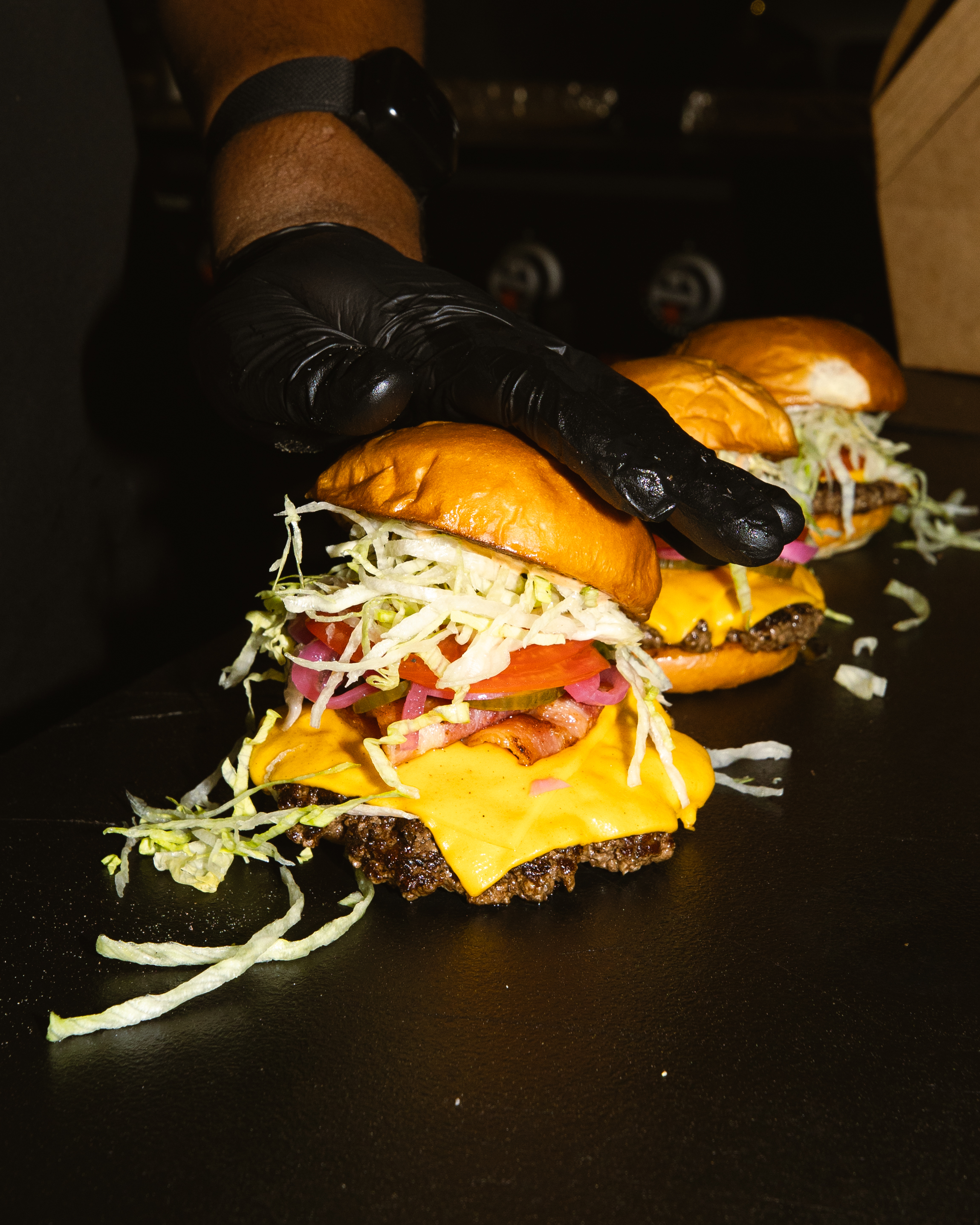 Joseph Boudreaux puts a bun on a smash burger topped with lettuce, tomato, and American cheese.