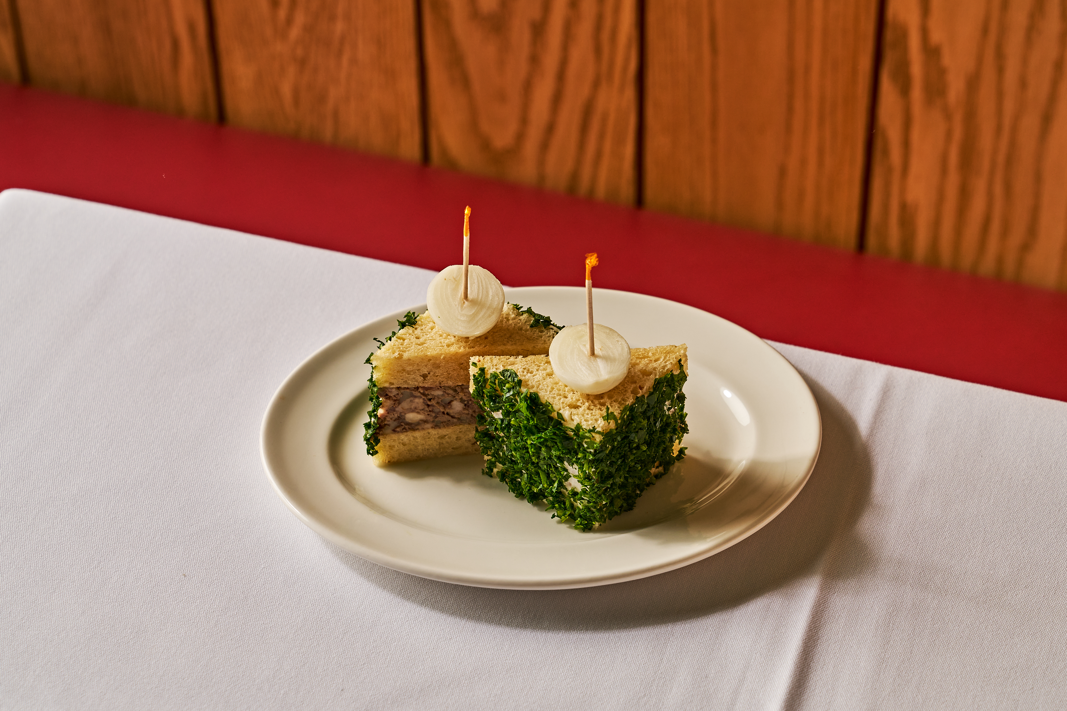 A plate with thick sandwich halves with one covered in green herbs on a white tableclothed table.