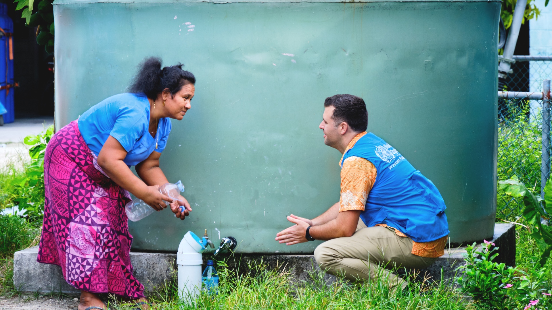 A WHO field staff talks to a woman fetching water from a water catchment tank.