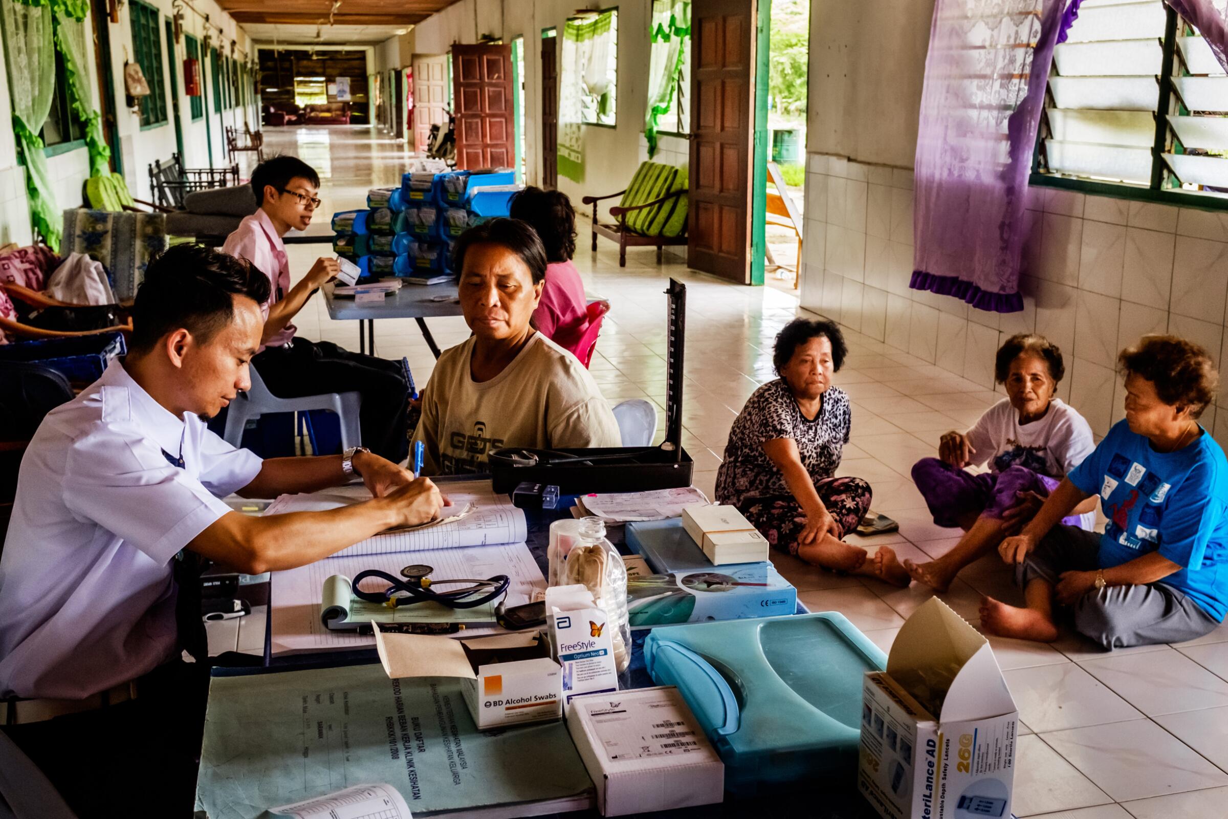 Healthcare workers attend to a group of women in a corridor setting.