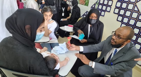 A man in a suit holds up a tiny figure for a baby to look at as he interacts with the mother.