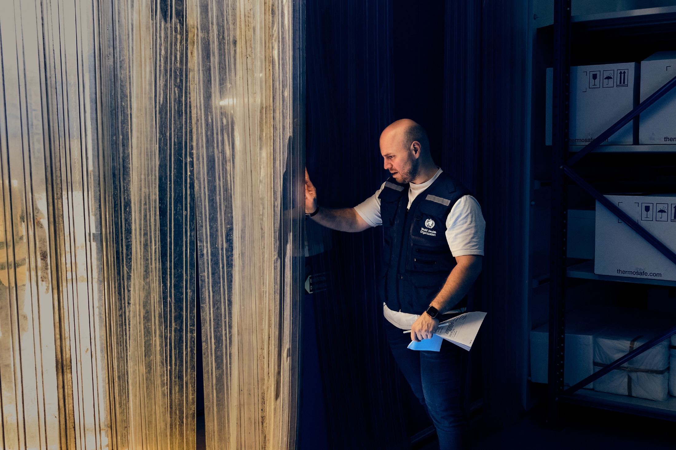 A WHO officer is about to walk through a plastic curtain to enter the temperature-controlled section of a warehouse.