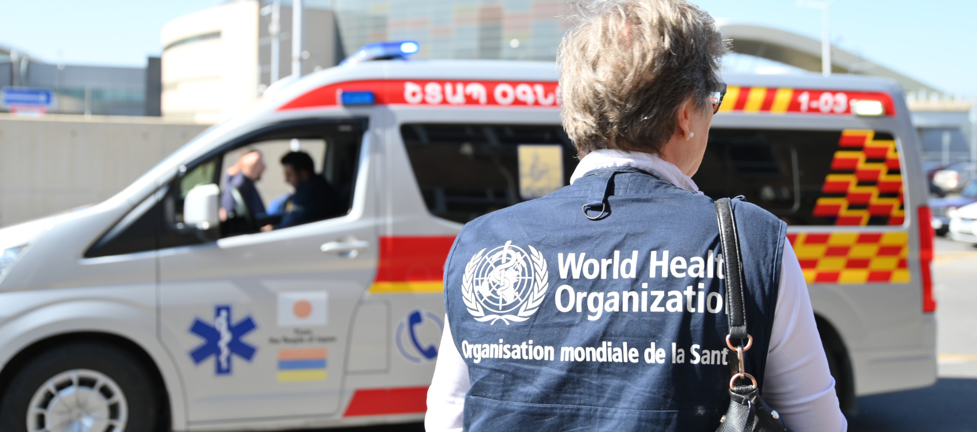 a world health organization professional santing in front of an ambulance