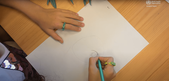 A sheet of paper on a table and the hands of a girl drawing a face on it