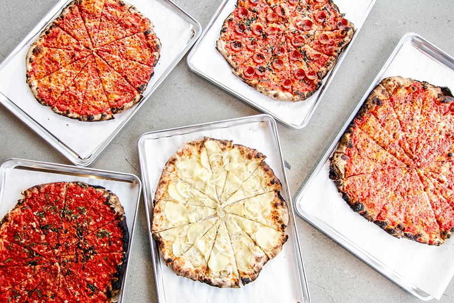 Overhead view of five different pizzas, each on its own metal tray.