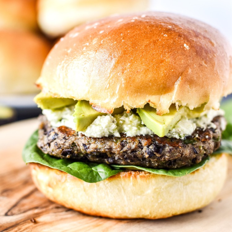 spicy black bean burgers with avocado and pesto goat cheese on a bun.