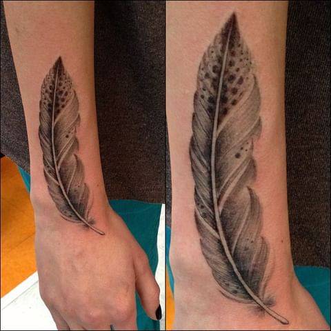 Black and grey style feather tattoo located on the forearm.