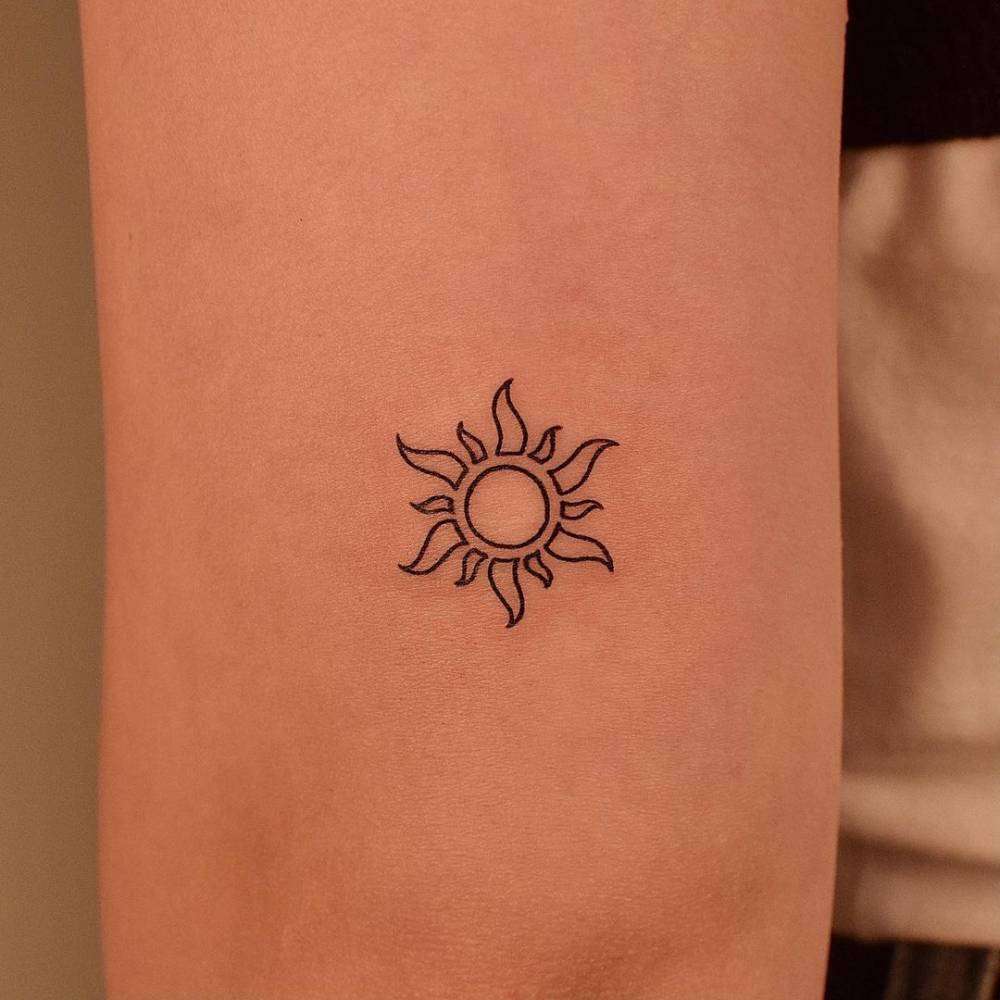 Minimalist sun tattoo on the tricep.