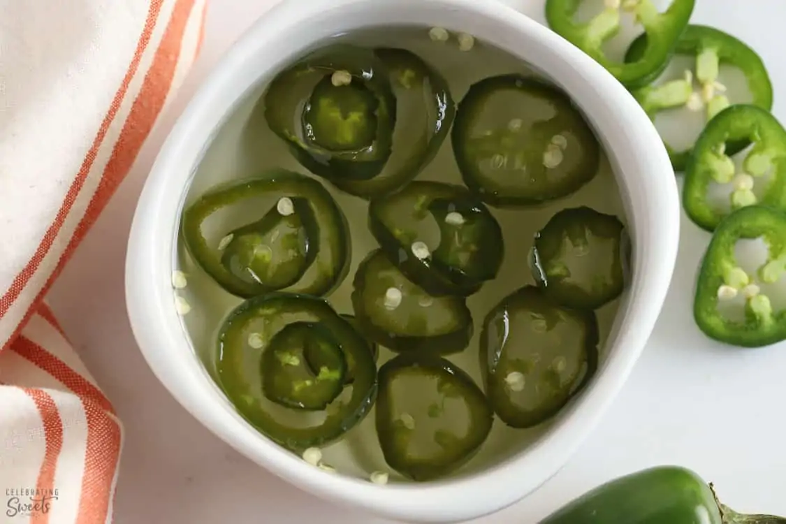 Jalapeno simple syrup in a white bowl next to an orange and white napkin.