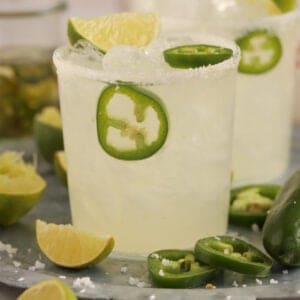 Spicy Margarita in a glass on a tray garnished with lime and jalapeno slices.