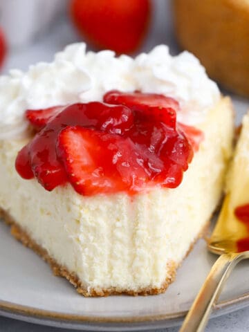 A slice of Greek yogurt cheesecake on a grey plate with a gold fork.