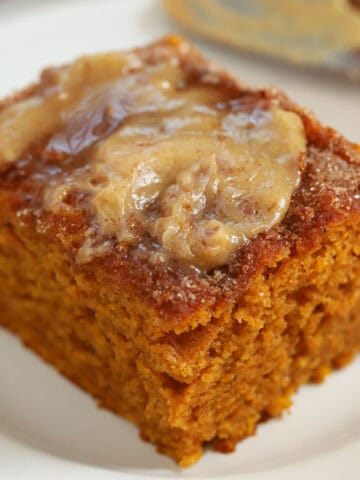 Slice of pumpkin cake topped with honey butter on a white plate.