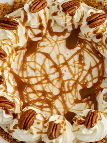 Overhead photo of a pecan pie cheesecake in a white pie plate decorated with caramel sauce and pecans.