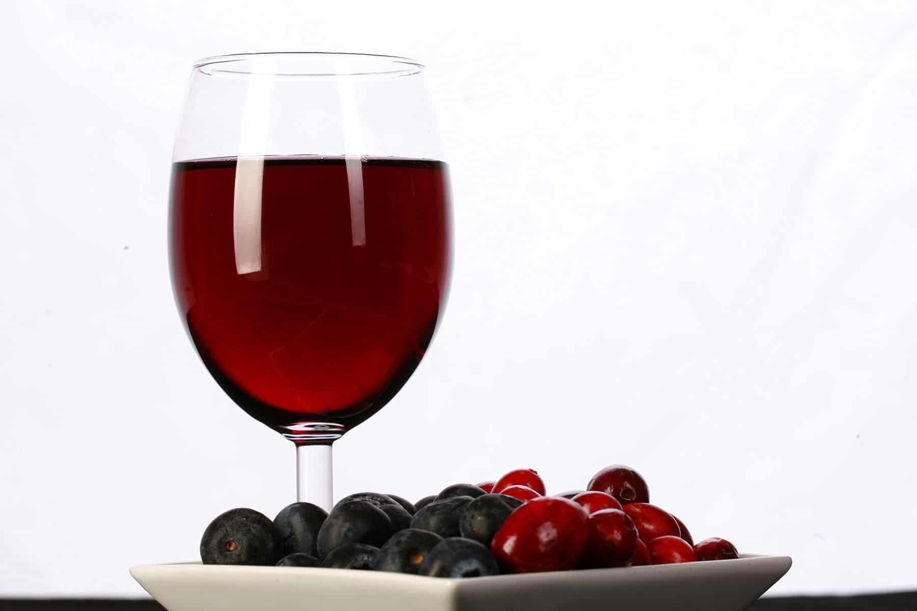 A glass of red wine is pictured next to a small bowl of cranberries and blueberries.