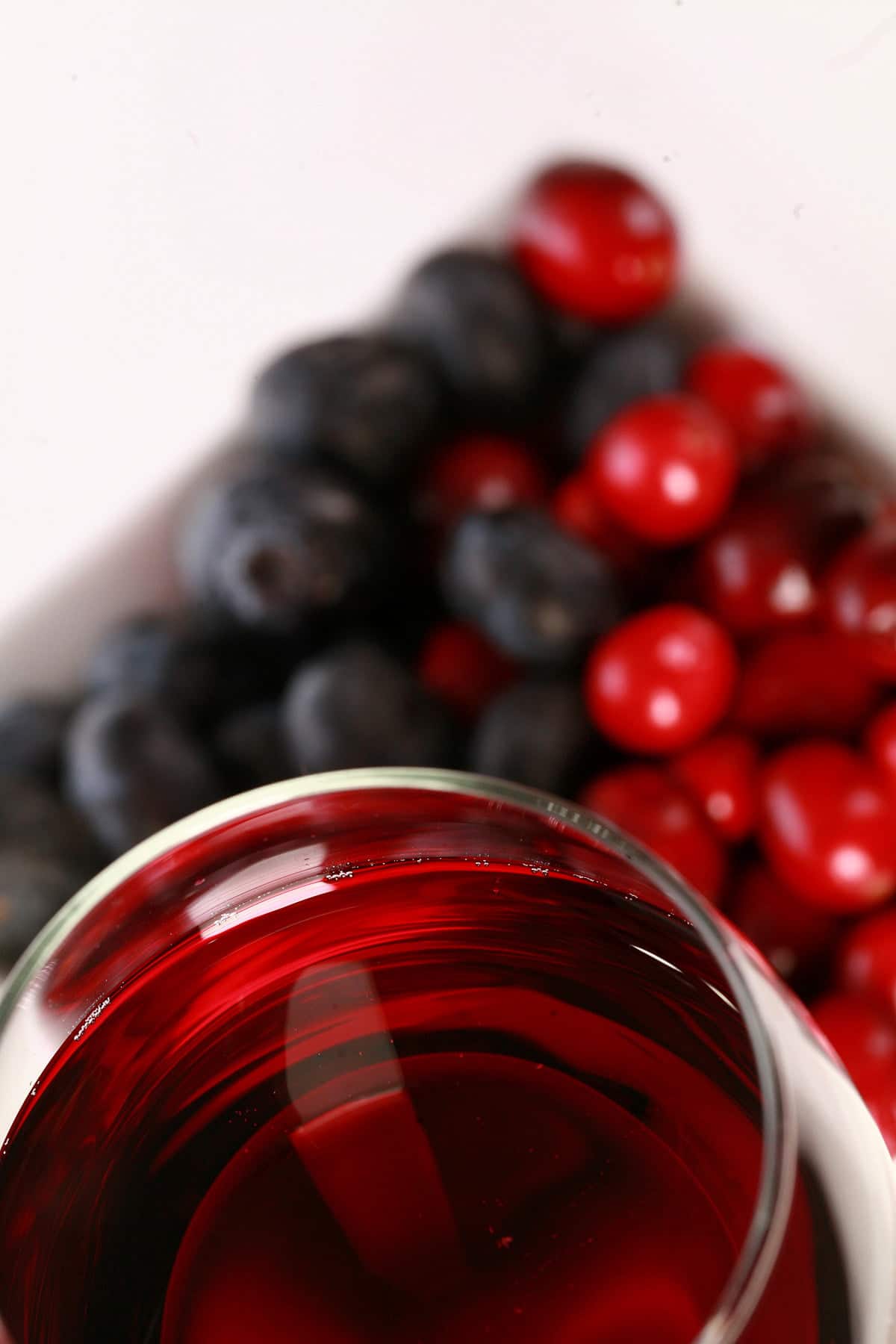 A glass of red wine - made from this faux lingonberry wine recipe - is pictured next to a small bowl of cranberries and blueberries