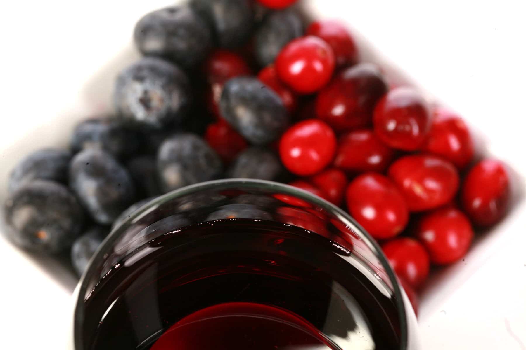 A glass of red wine is pictured next to a small bowl of cranberries and blueberries.