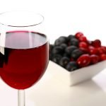 A glass of red wine is pictured next to a small bowl of cranberries and blueberries.