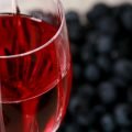 A faceted wine glass full of blueberry mead, with fresh blueberries behind the glass.