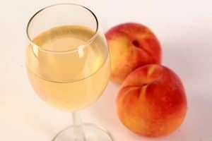 A glass of pale peach coloured wine, with 2 fresh peaches at the base of the glass.