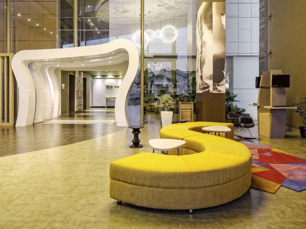 a lobby with a yellow bench and tables in a building at Ibis Padang in Padang