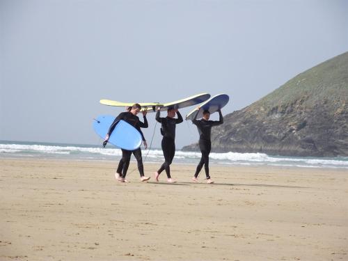 three people walking on the beach with surfboards on their backs at Trevarrian Lodge in Newquay