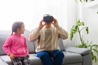 Senior man wearing virtual reality goggles at home with granddaughter by his side