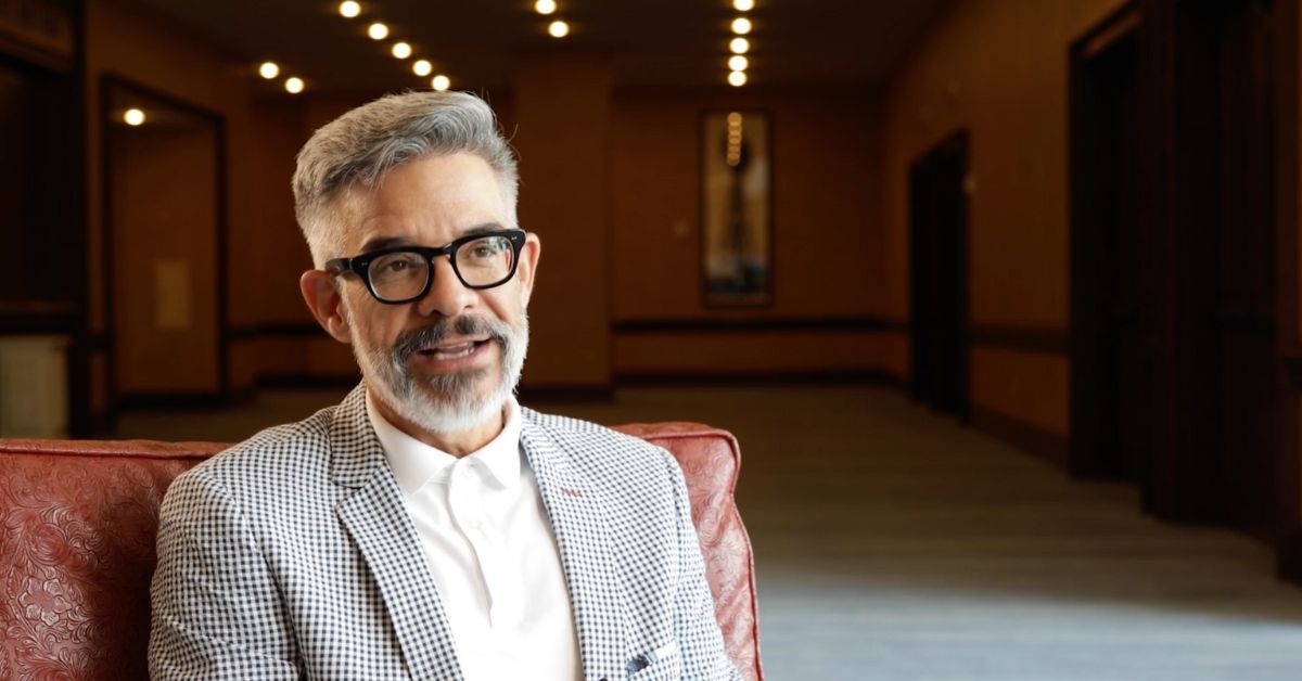 Dr. Adam Sáenz smiles as he addresses the camera in a formal interview setting