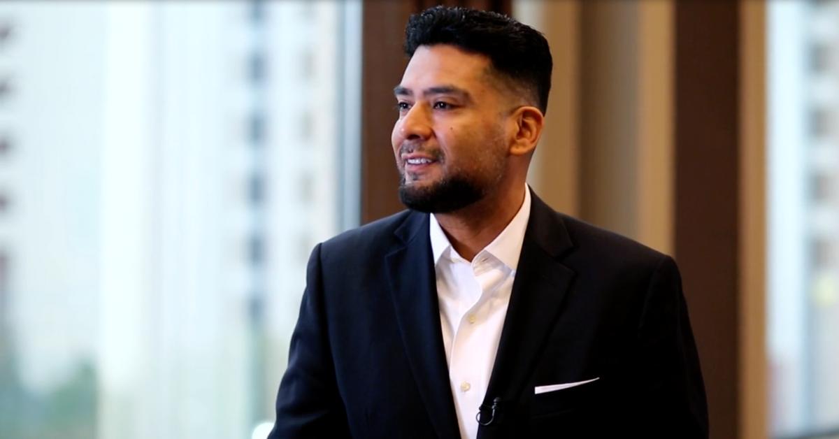 Dr. Victor Rios sits in front of a large window and smiles during a formal interview