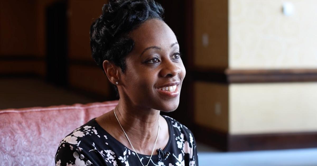 Monica Washington smiles as he addresses the camera in a formal interview setting