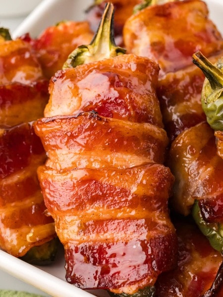 Closeup of a pile of Bacon Wrapped Jalapeño Poppers on a white plate.