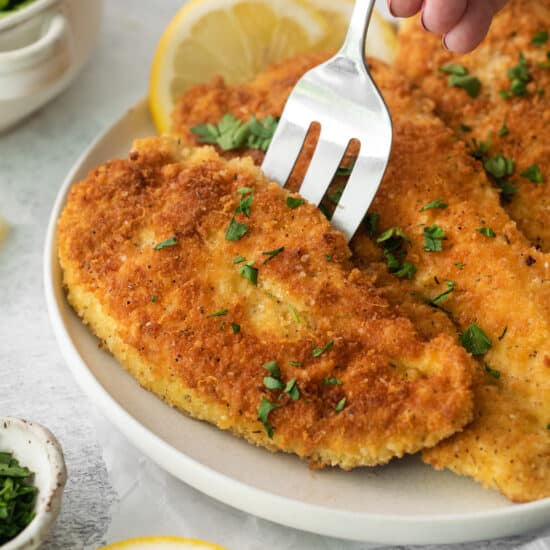 a person holding a fork on a plate of lemon chicken.