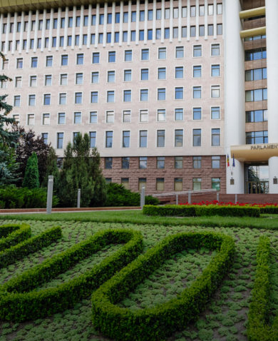 The front of Moldovan parliament with green hedging cut into the word "Moldova" in the foreground.