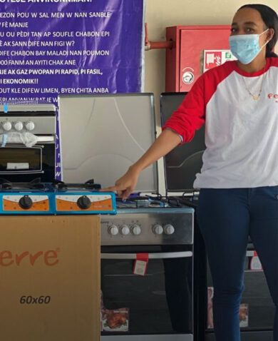 A woman wearing a protective mask stands beside several gas stoves on display in a store.