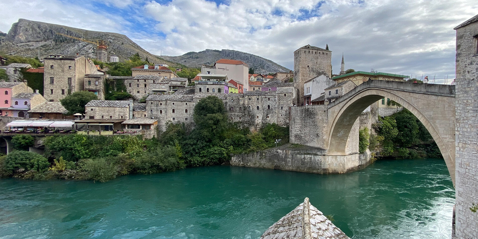 Image of a large town on a river with a bridge going across. Mountains can be seen in the distance.